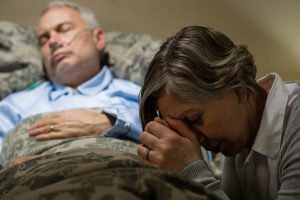 Senior woman praying for sick man sleeping in hospital bed