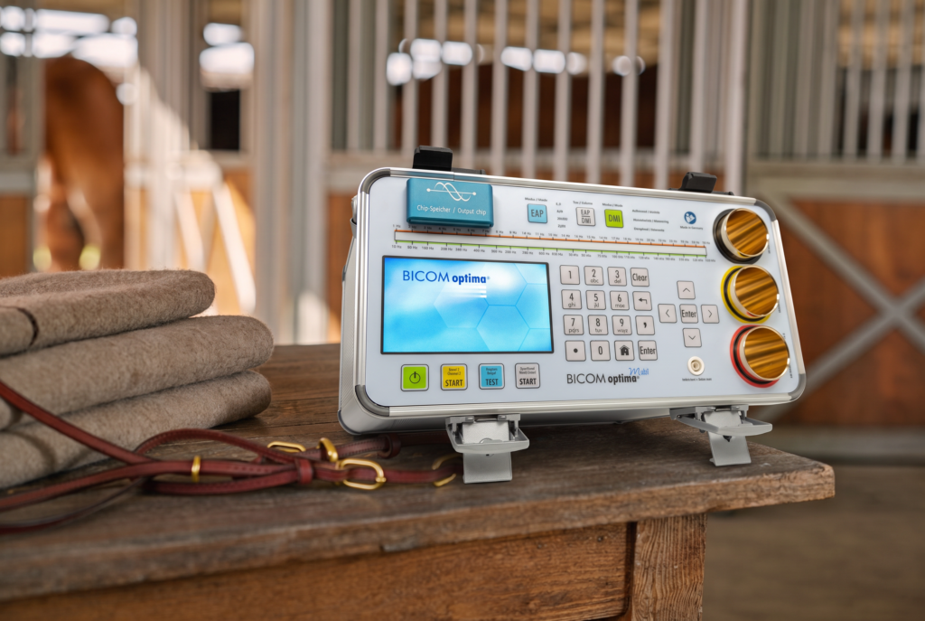 The BICOM optima mobile control panel on a tack room table beside folded blankets and a leather bridle